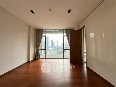 Spacious empty room with wooden floor and city view through large windows.