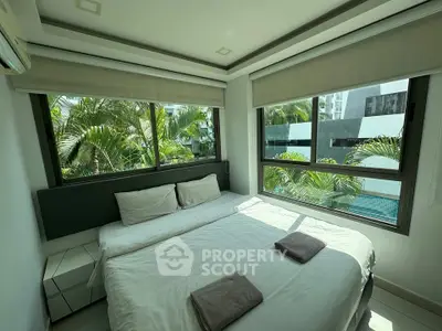 Modern bedroom with large windows and pool view, featuring a cozy bed and lush greenery outside.