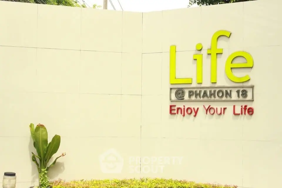 Modern real estate development sign with vibrant greenery and inviting message.