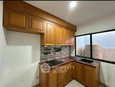Charming kitchen with wooden cabinets and colorful backsplash, featuring a sleek black countertop and large window.