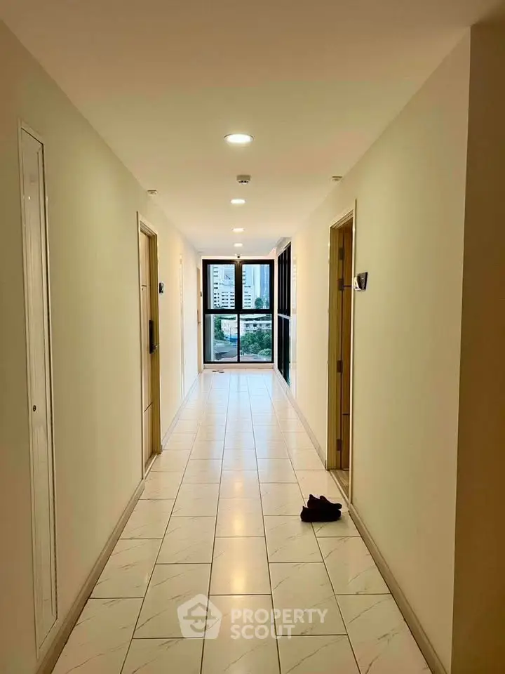 Bright corridor with tiled flooring leading to a window with city view in a modern building.