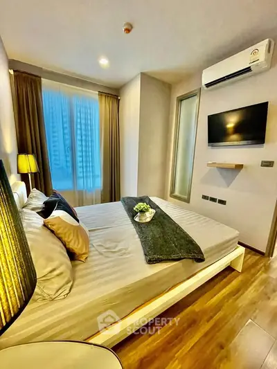Modern bedroom with cozy lighting, sleek wooden flooring, and wall-mounted TV in a stylish apartment.