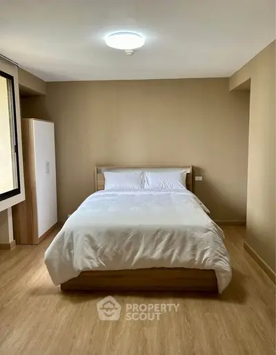 Cozy bedroom with wooden flooring and minimalist decor, featuring a comfortable bed and ample natural light.