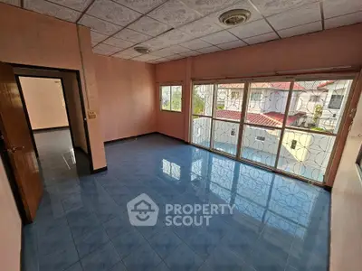 Spacious living room with large windows and blue tiled floor, offering ample natural light and a view of neighboring rooftops.