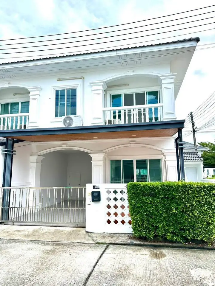 Charming two-story white house with lush greenery and gated entrance in a serene neighborhood.