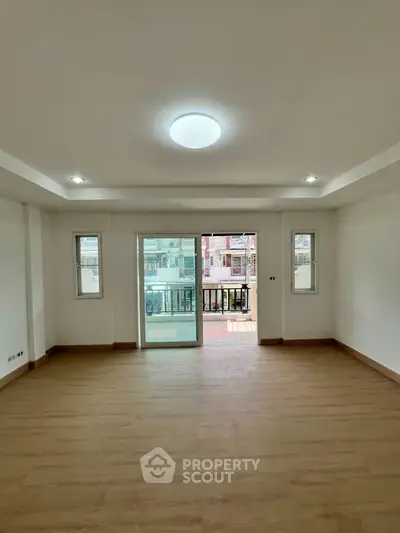 Spacious empty living room with wooden flooring and balcony access in modern apartment.