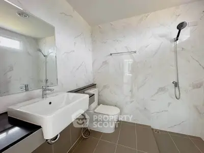 Modern bathroom with sleek fixtures and elegant marble walls, featuring a spacious shower area and contemporary sink.