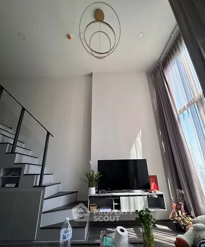 Modern living room with high ceiling and stylish staircase, featuring a large window with natural light.