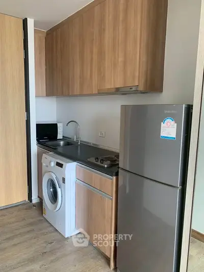 Modern kitchen with wooden cabinets, washing machine, and stainless steel fridge