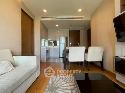 Modern open-plan living room with kitchen and dining area, featuring sleek furniture and wooden flooring.