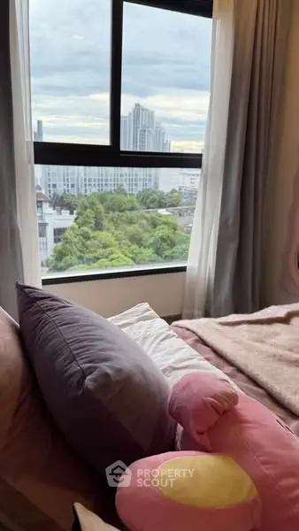 Cozy bedroom with plush pillows and city view from large window.