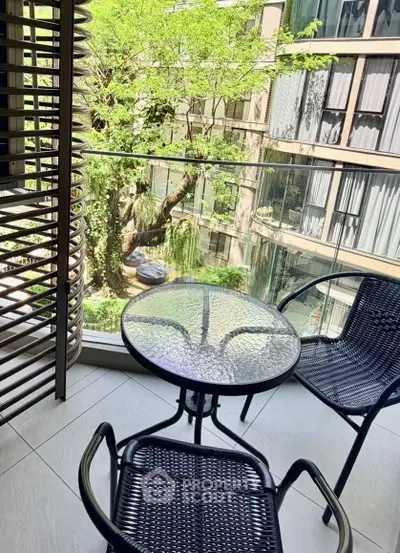 Charming balcony with glass railing and outdoor seating overlooking lush greenery.