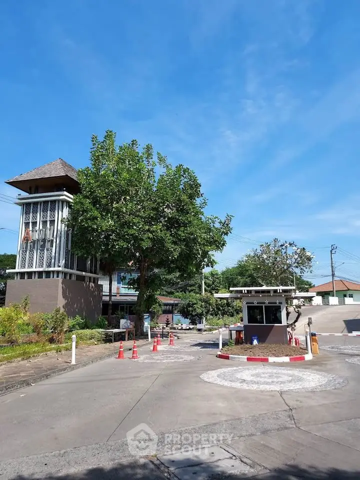 Charming residential entrance with security booth and lush greenery under clear blue sky.