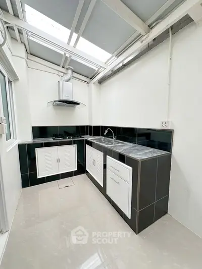 Modern kitchen with sleek black and white design, featuring gas stove and ample natural light.