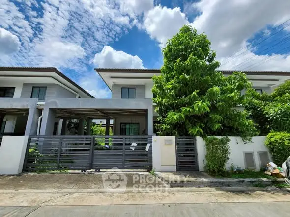Modern two-story house with lush greenery and a sleek metal gate under a bright blue sky.