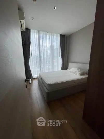 Modern bedroom with large window and city view, featuring sleek wooden flooring and minimalist design.