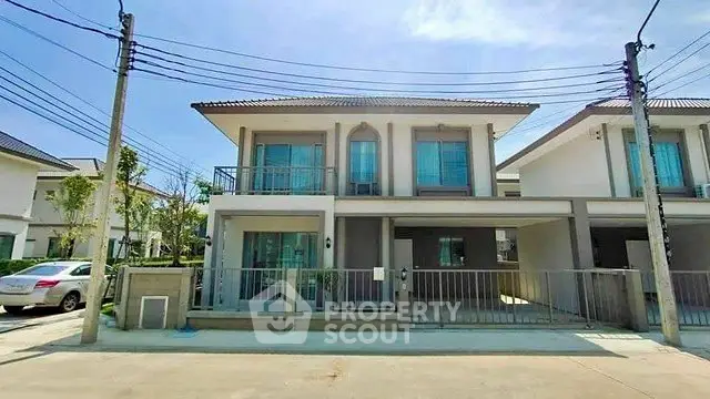 Modern two-story house with balcony and driveway in a suburban neighborhood.