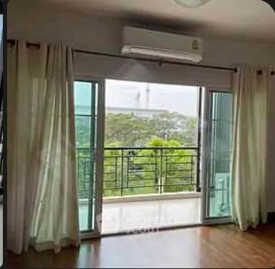 Spacious living room with large windows and balcony offering a serene view of greenery.