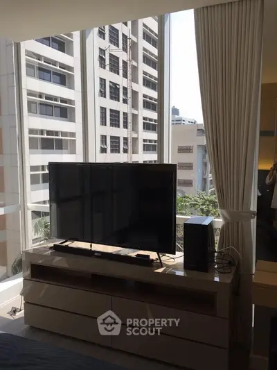 Modern living room with large windows and city view, featuring sleek TV setup.