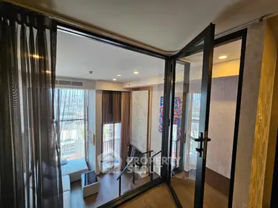 Modern living room with floor-to-ceiling windows and balcony access, offering stunning city views.