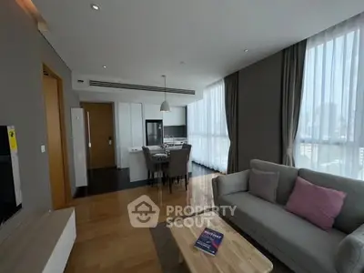Modern living room with open kitchen and dining area, featuring elegant decor and large windows.