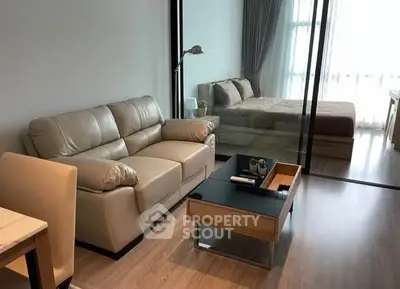 Modern living room with leather sofa and glass partition leading to cozy bedroom.