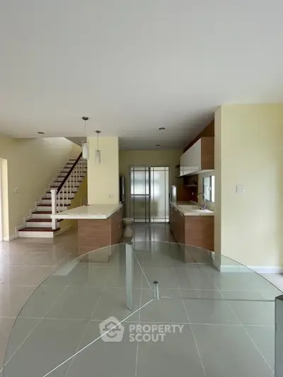 Modern open kitchen with sleek design and staircase, featuring glass dining table and ample natural light.