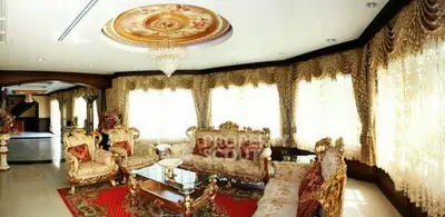 Luxurious living room with ornate furniture and elegant drapery, featuring a stunning chandelier and intricate ceiling design.