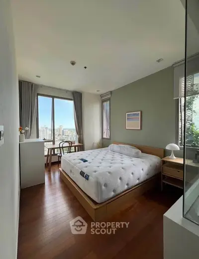 Spacious bedroom with large windows offering stunning city views, featuring a cozy bed and elegant wooden flooring.