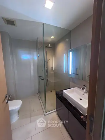 Modern bathroom with glass shower and sleek fixtures in contemporary apartment.