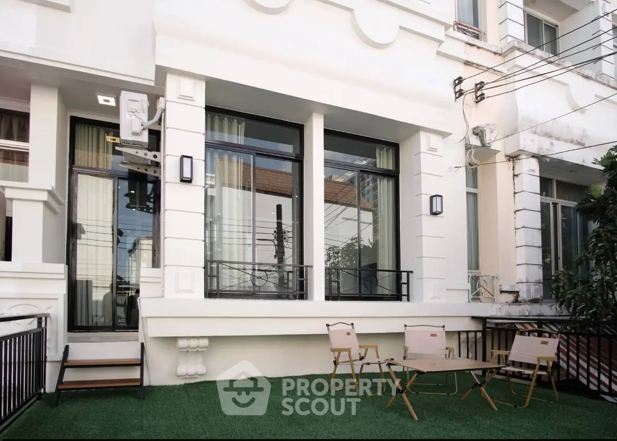Charming townhouse exterior with cozy outdoor seating area on artificial grass lawn.