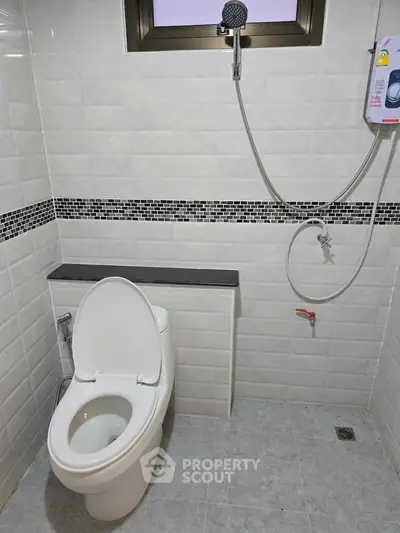 Modern bathroom with white tiles and showerhead, featuring a sleek toilet design.