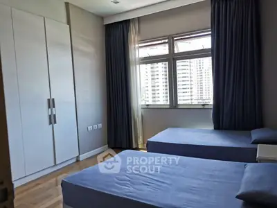 Spacious bedroom with twin beds and city view, featuring large windows and ample closet space.