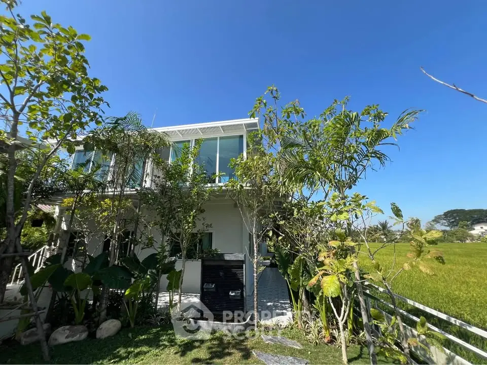 Modern two-story house with lush garden and clear blue sky, perfect for nature lovers seeking tranquility.