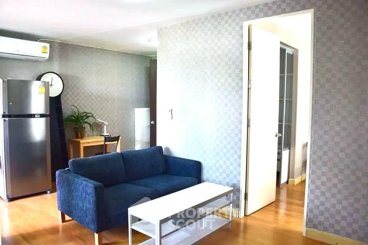 Modern living room with blue sofa, white table, and sleek kitchen appliances.