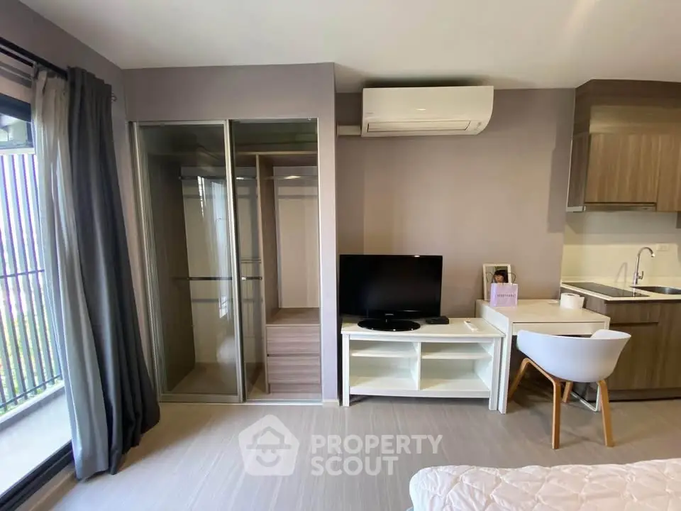 Modern studio apartment with sleek design, featuring a compact kitchen, TV area, and large window for natural light.