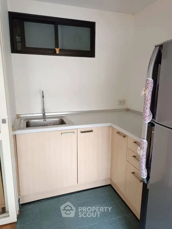 Compact kitchen with light wood cabinets and stainless steel fridge