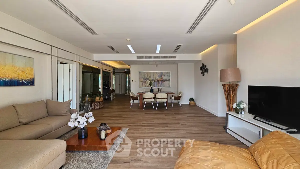 Spacious modern living room with elegant decor and open dining area, featuring stylish furniture and warm lighting.