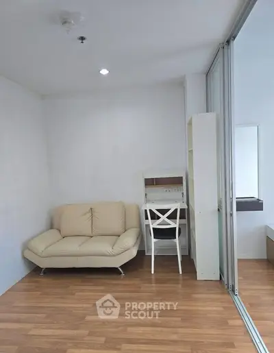 Modern living room with cozy beige sofa and compact study area, featuring sleek wooden flooring and bright lighting.