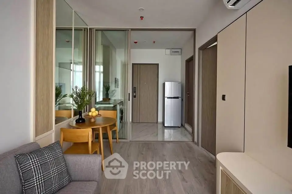 Modern living room with sleek design, featuring a cozy sofa, dining area, and compact kitchen with stainless steel fridge.