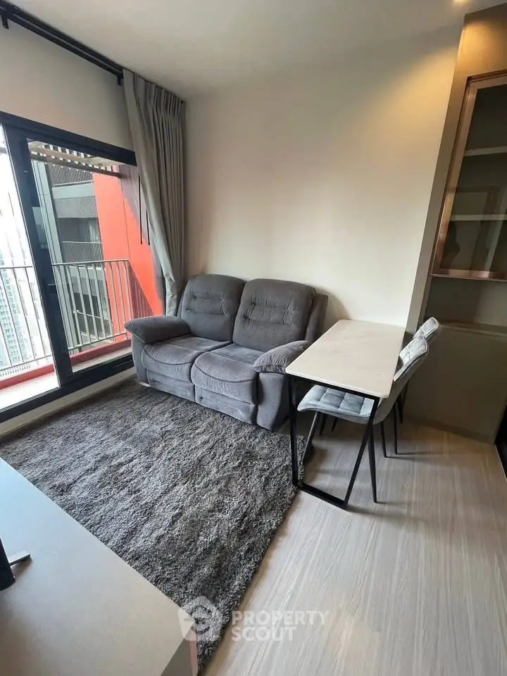 Modern living room with cozy gray sofa, stylish table, and balcony view in urban apartment.