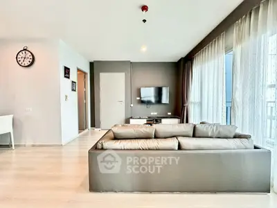 Modern living room with sleek sofa and wall-mounted TV, featuring large windows and elegant decor.