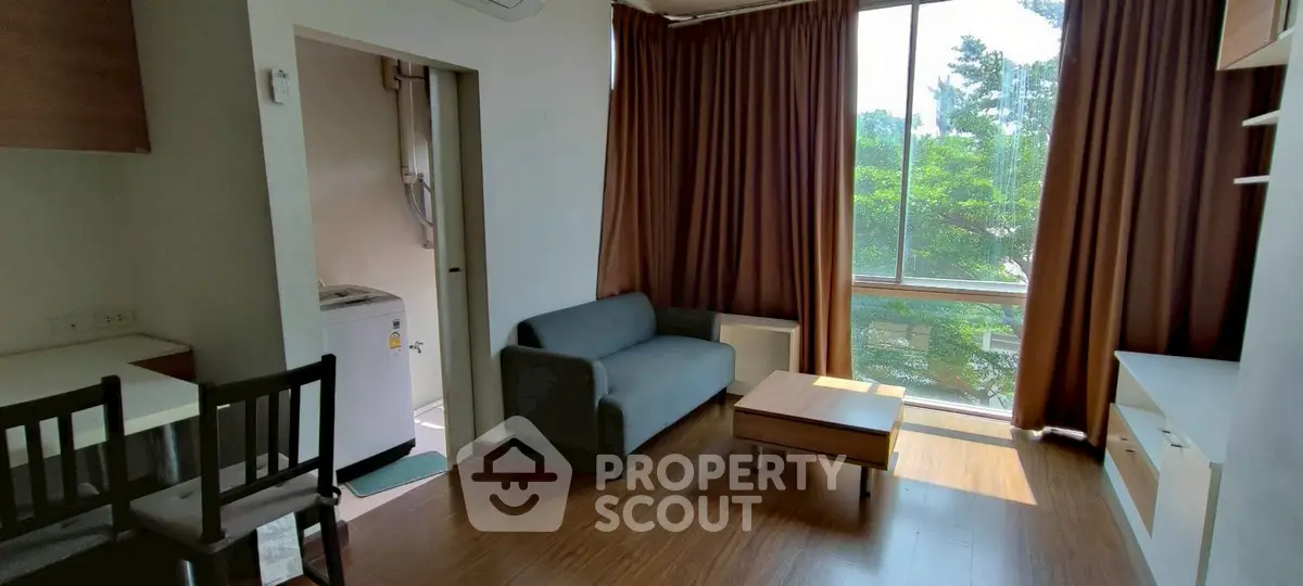 Cozy living room with large window and natural light, featuring a sofa and wooden flooring.