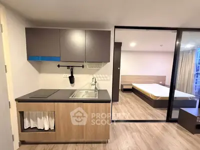 Modern studio apartment with compact kitchen and sliding glass partition to bedroom.