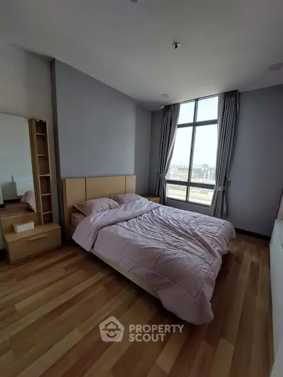 Spacious bedroom with large window and wooden flooring in modern apartment