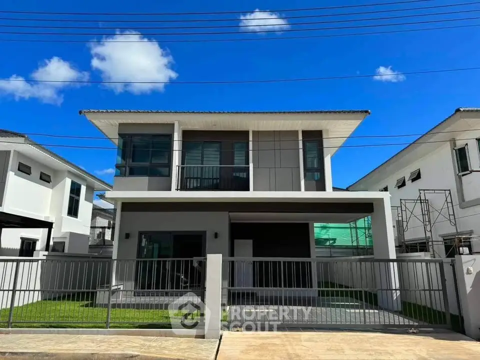 Modern two-story house with sleek design and spacious front yard under clear blue sky.