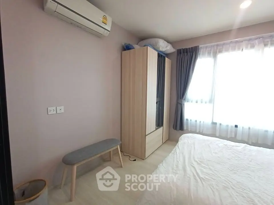 Cozy bedroom with natural light, featuring a wardrobe, air conditioning, and a comfortable bed.