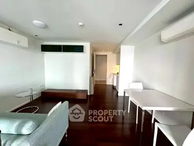 Modern minimalist living room with sleek furniture and open layout, featuring dark wood flooring and bright lighting.