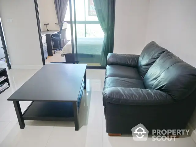 Modern living room with sleek black leather sofa and glass coffee table, adjacent to a cozy bedroom.