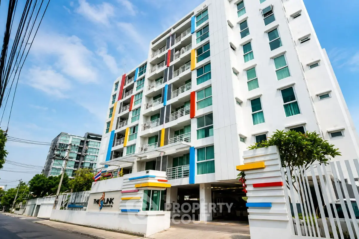 Modern multi-story apartment building with colorful accents and gated entrance in urban setting.